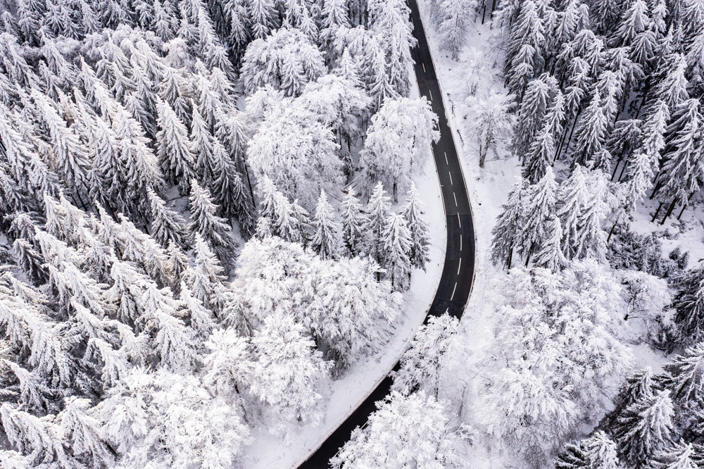 A stunning aerial shot of a snow-covered road in the Taunus' Feldberg forest, captured in exquisite detail by the Mavic 2 Pro drone