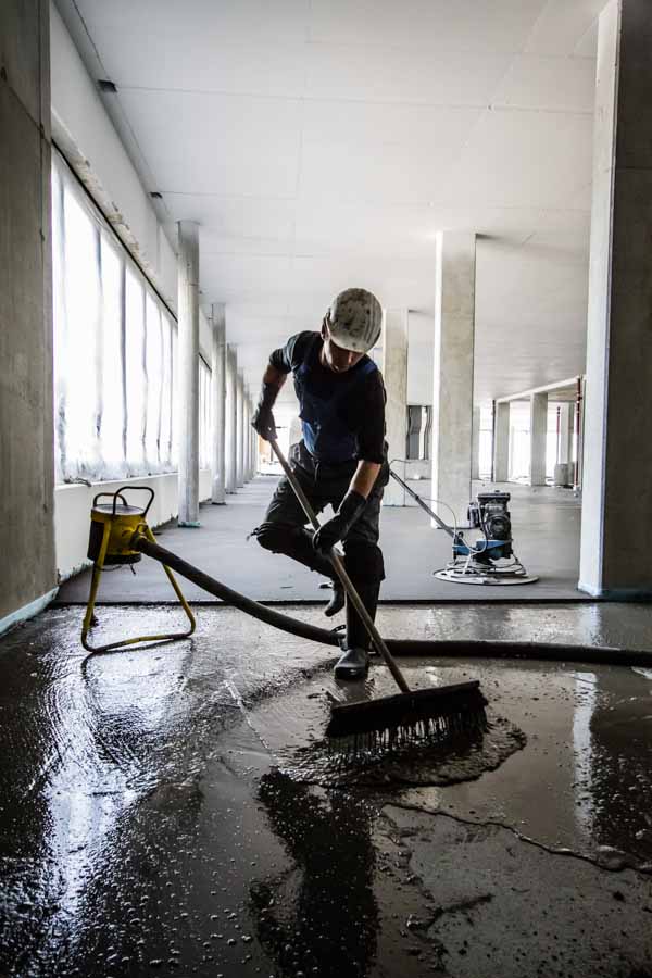 A craftsman spreads floor adhesive with a broom on the Clariant Innovation Center construction site